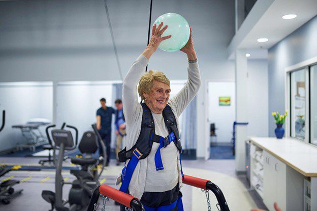 Woman in physical therapy holding up ball above head
