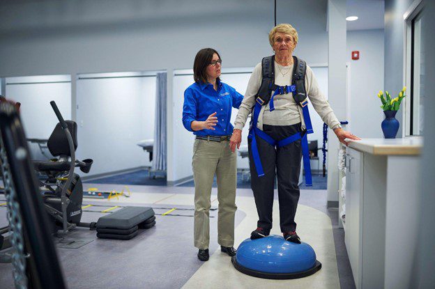 A Physical therapist helps a woman with a bosu ball in a harness