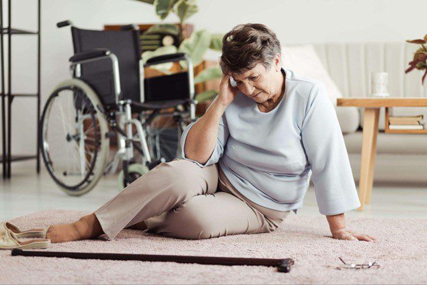 an elderly woman sits on the floor after falling touching her head