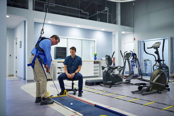 a man in a harness practices putting a golf ball during physical therapy
