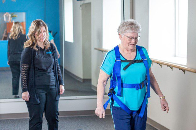 A woman walks under the supervision of a physical therapist