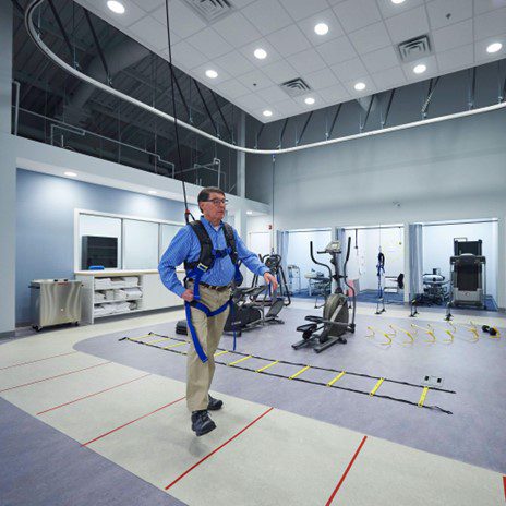 A man practices a gait exercise while using an overhead harness